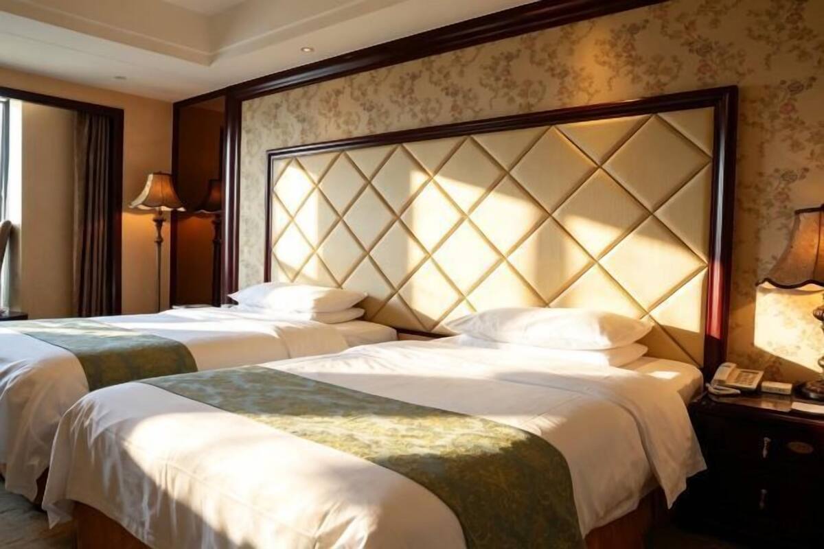 A hotel room with two beds, a large padded headboard, a bedside lamp, and a telephone on the nightstand.
