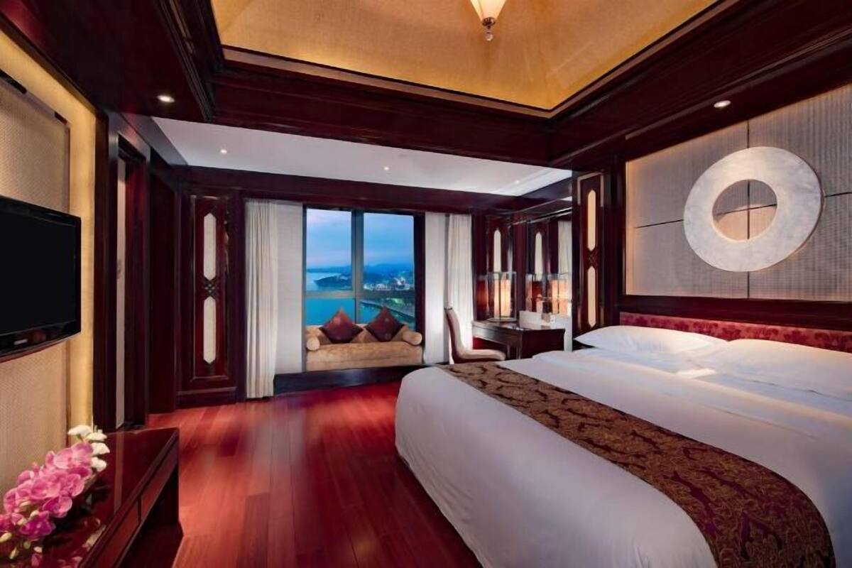 A hotel room with a large bed, a TV, a desk, and a view of the city.
