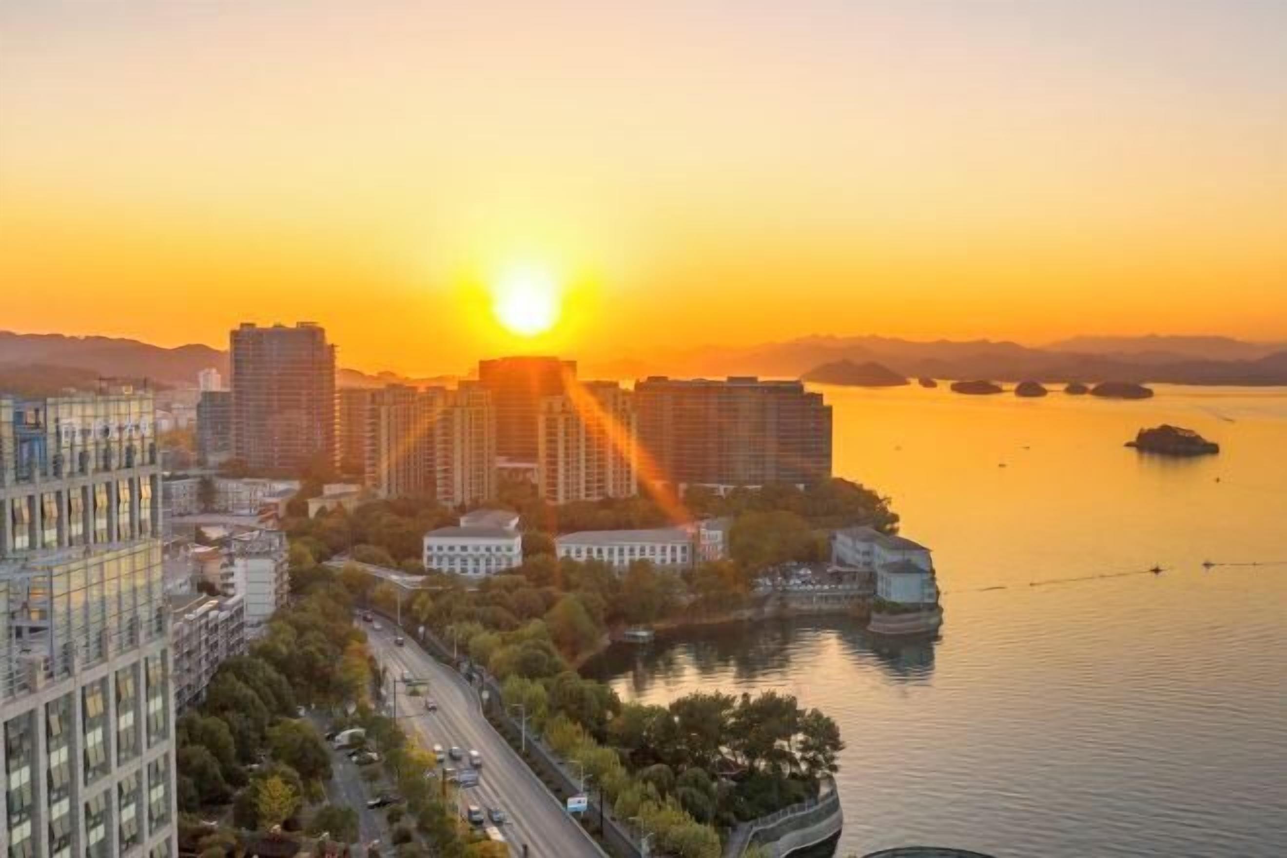 Paisagem urbana ao pôr do sol, com arranha-céus, um rio e uma pequena ilha.