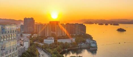 Paisagem urbana ao pôr do sol, com arranha-céus, um rio e uma pequena ilha.