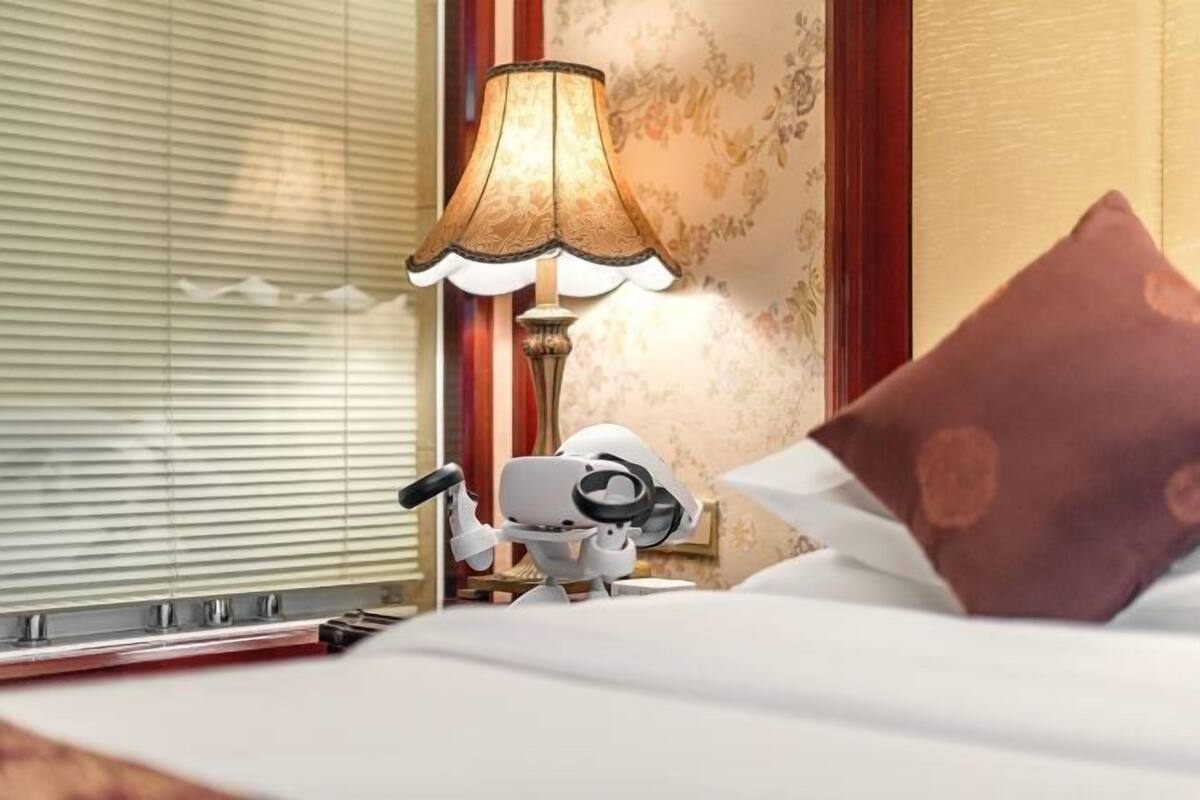A hotel room with a bed, a lamp, and a wall with floral wallpaper.