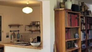 A living room with a wooden staircase, a kitchen area, and a bookshelf. - Maison Sarzeau / Saint Gildas de Rhuys (Sarzeau)
