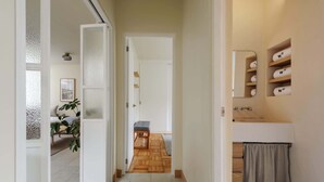 A hallway with a wooden floor, a bench, and a door leading to a room with a bed and a plant. - w* | Captivating 2BR with Balcony  in Roma Norte (Ciudad de México)