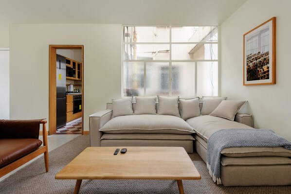 Una sala de estar moderna con un sofá, una mesa de centro y vista a la cocina a través de una puerta de cristal.