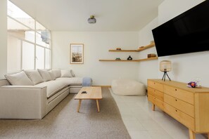 Una sala de estar moderna con un sofá modular, una mesa de centro de madera, un televisor en la pared y un mueble de madera.