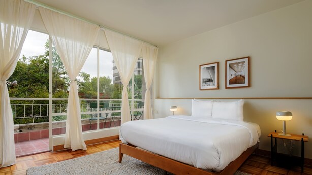 A bedroom with a wooden bed, white bedding, a balcony with a railing, and two framed pictures on the wall. - w* | Captivating 2BR with Balcony  in Roma Norte (Ciudad de México)