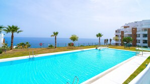 A swimming pool with clear blue water, surrounded by palm trees and a view of the ocean. - Luxury Premium Isea 1122 by Casasol (Torrox Costa)