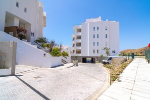 Een modern gebouw met een witte gevel, meerdere balkons en een verhard terras met een kleine tuin.