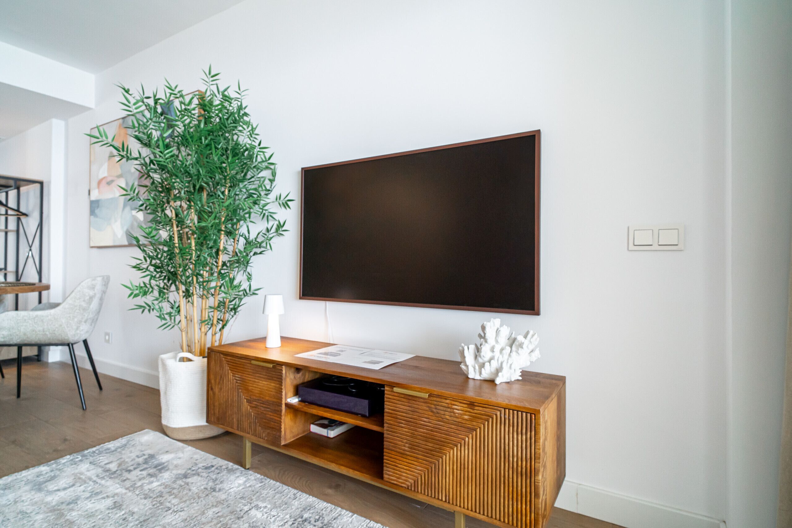 A modern living room with a large flat-screen TV mounted on the wall, a wooden console table with a plant, and a minimalist design.