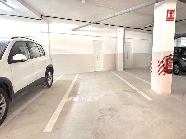 Een parkeergarage met witte muren, genummerde parkeerplaatsen en een brandblusser bevestigd aan een pilaar.