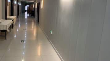 A hotel corridor with tables and chairs on the left, a clean floor, and a lighted wall on the right.