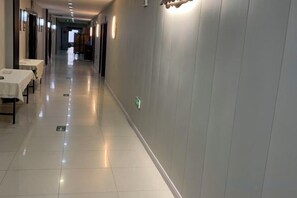 A hotel corridor with tables and chairs on the left, a clean floor, and a lighted wall on the right. - Riron International Hotel (Binhai)