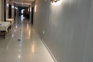 A hotel corridor with tables and chairs on the left, a clean floor, and a lighted wall on the right.