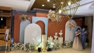 A decorated indoor space with a stage, floral arrangements, and a ceiling light fixture.