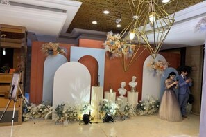 A decorated indoor space with a stage, floral arrangements, and a ceiling light fixture.