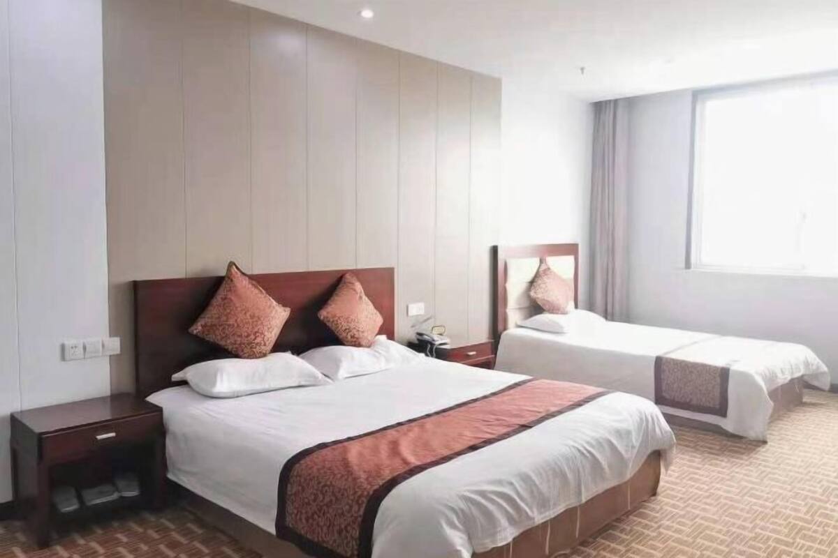 A hotel room with two beds, a wooden headboard, a nightstand, and a large window.