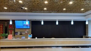 Una hall d'albergo dal design moderno, con una reception, uno schermo digitale e illuminazione a sospensione.