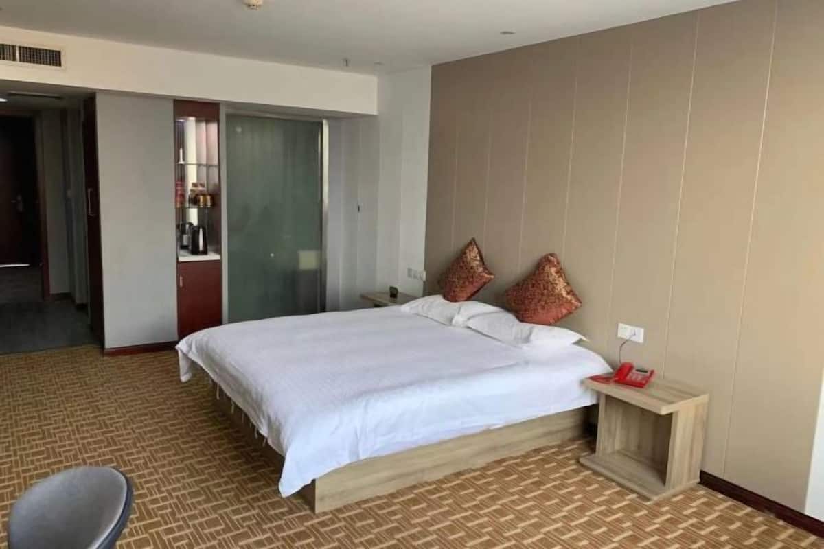 A hotel room with a large bed, a bedside table with a lamp, a chair, and a wardrobe.