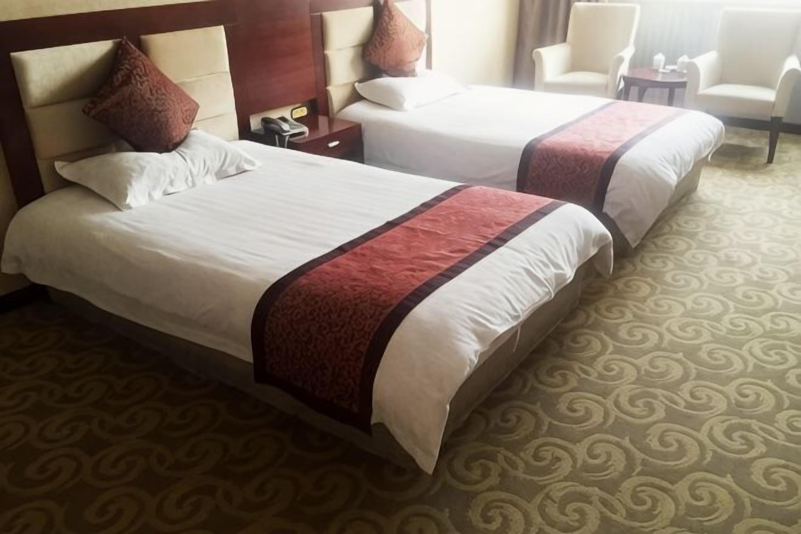 Two beds with white linens and brown accents, a patterned carpet, and a wooden headboard.