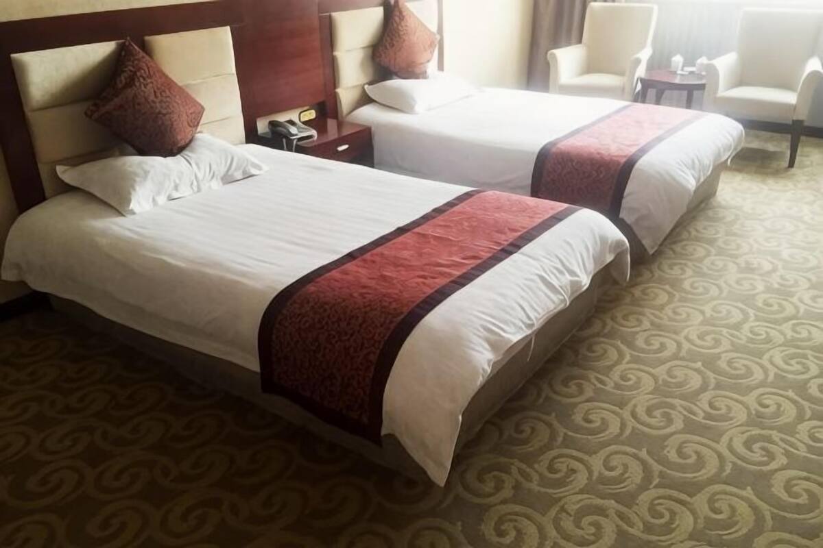 Two beds with white linens and brown accents, a patterned carpet, and a wooden headboard.