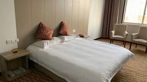 Camera d'albergo con un letto, due cuscini, un comodino con il telefono, una sedia e una finestra.