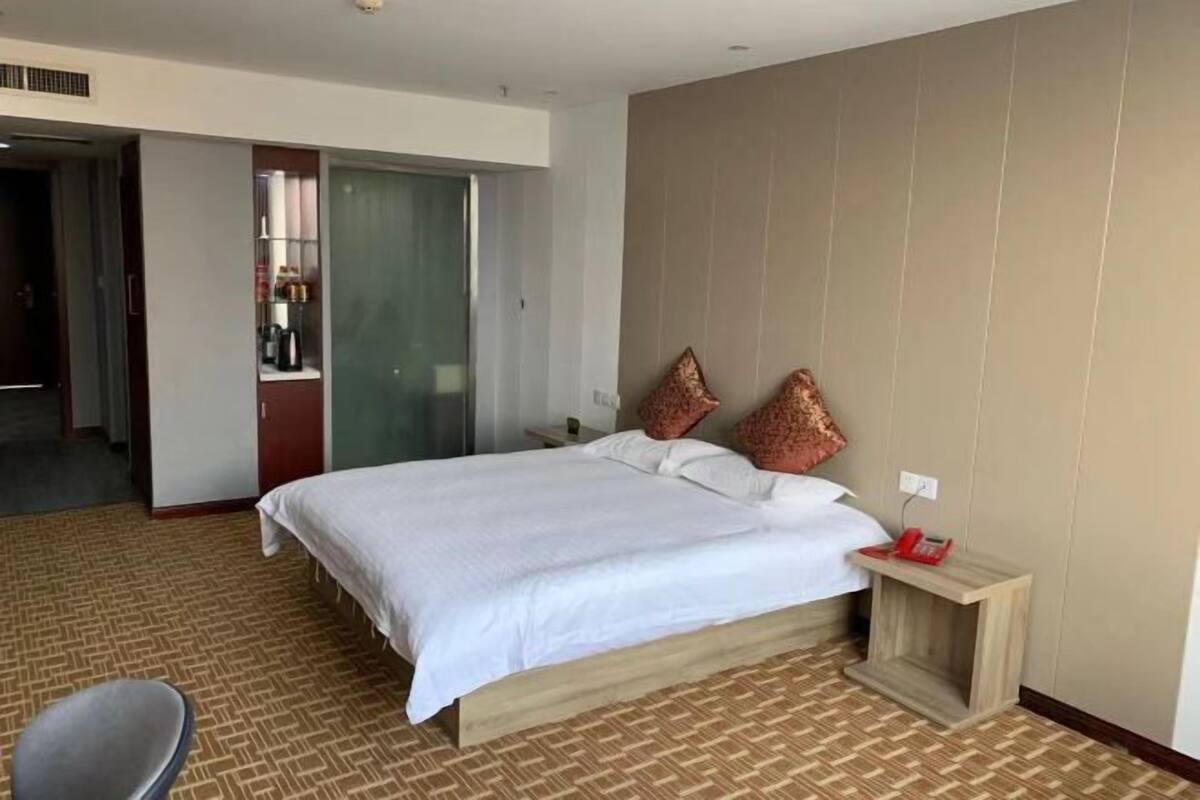 A hotel room with a bed, a bedside table, a chair, and a wardrobe.