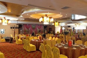 A banquet hall with round tables, yellow chairs, and chandeliers.