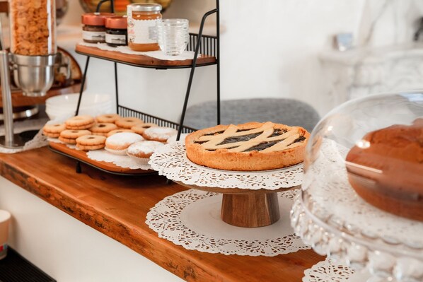 A wooden counter with various baked goods, including a pie and cookies, and a cake on a stand. - Executive B&B (Scafa)