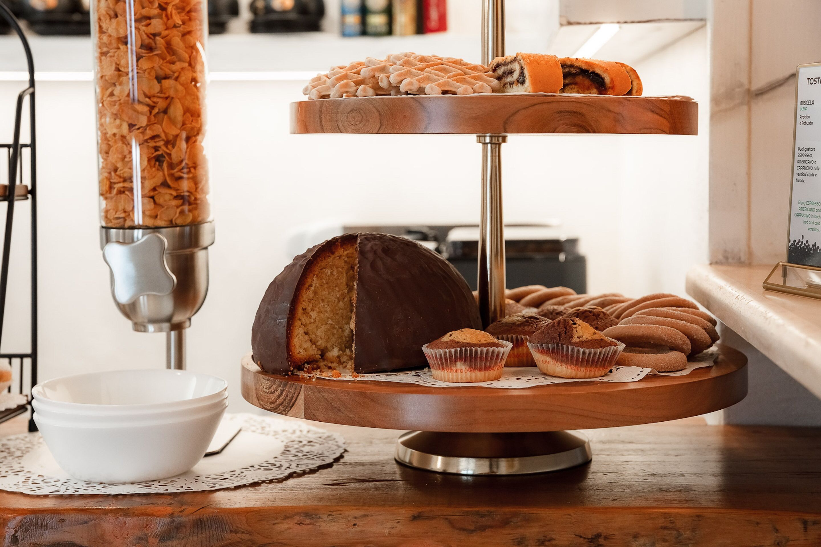 A wooden serving tray with pastries and a chocolate cake on a table.
