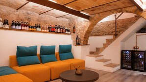 Un interior acogedor con pared de piedra, una escalera de madera, un sofá con cojines color turquesa y un refrigerador para vino.