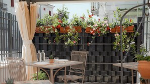 Un patio al aire libre con una mesa y sillas, rodeado de plantas en macetas y una valla negra.