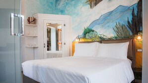 Un dormitorio con cama, armario blanco, cabina de ducha de vidrio y un mural en la pared.