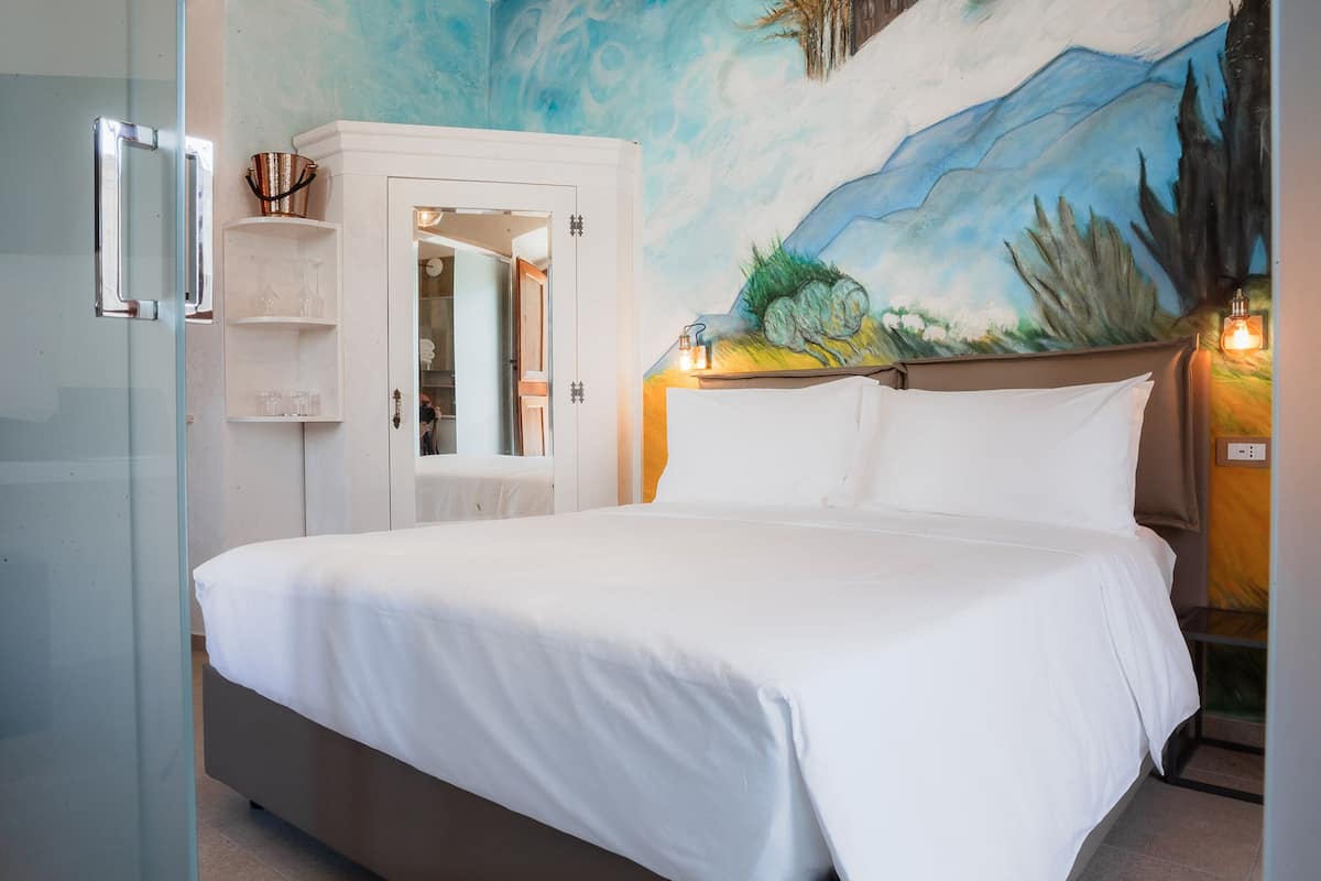 Un dormitorio con cama, armario blanco, cabina de ducha de vidrio y un mural en la pared.