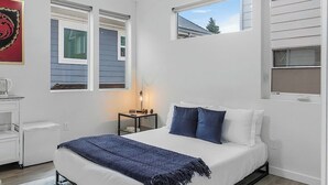 A bedroom with a bed, a nightstand, a lamp, and a window. - Vermithor's Bronze Ember Sweet Suite (Seattle)