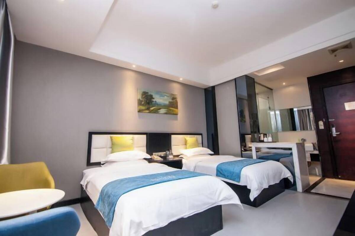 Habitación de hotel con dos camas, una mesita, una silla, un cuadro en la pared y un espejo.