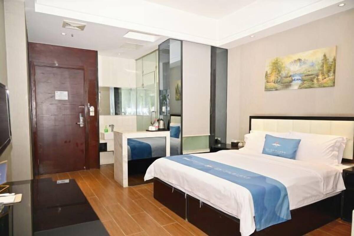 Habitación de hotel con cama, escritorio, espejo, un cuadro en la pared y una puerta.