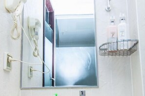 A bathroom with a hairdryer, a telephone, and a mirror. There are two bottles on the wall. - Yicheng Hotel (Henan University of Technology) (Zhengzhou)