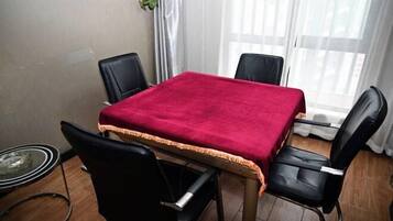 A room with a table covered by a red cloth, four black chairs, a glass table, and a window with curtains.