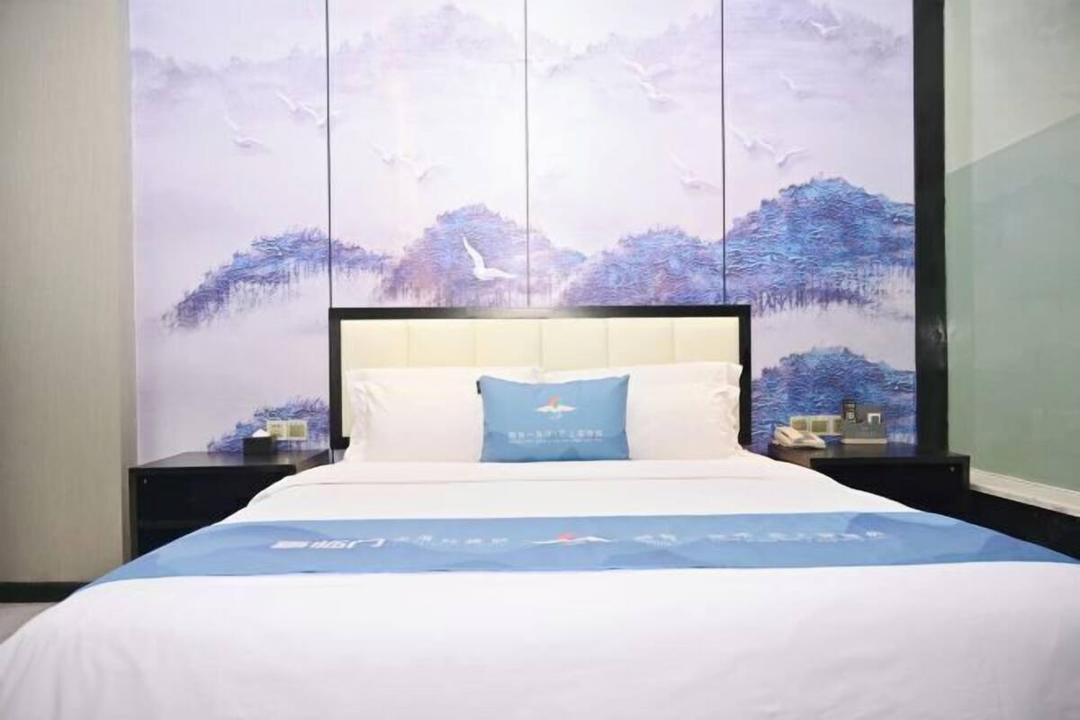 Una habitación de hotel con una cama grande, una mesita de noche y un mural temático de naturaleza en la pared.