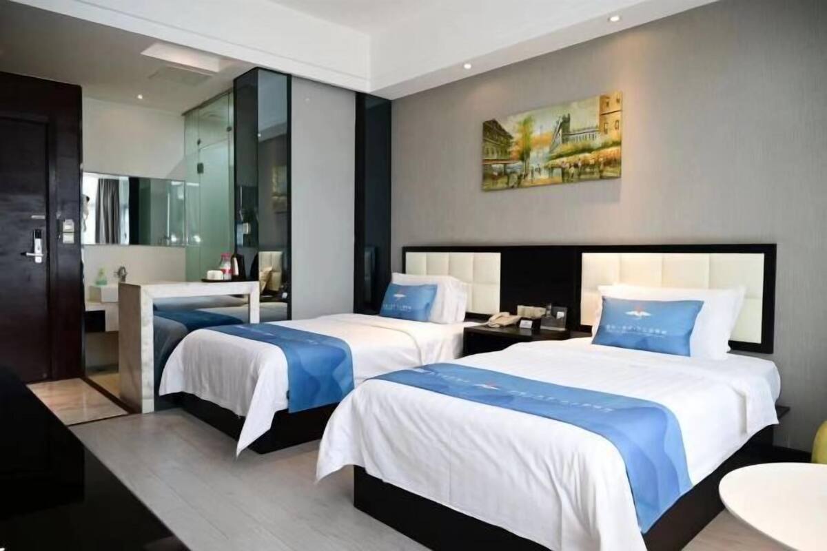 Habitación de hotel con dos camas, un escritorio, una silla y un cuadro en la pared.