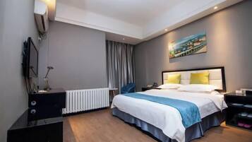 A modern hotel room with a large bed, a bedside table, a desk, a chair, a radiator, a painting on the wall, and a window with curtains.