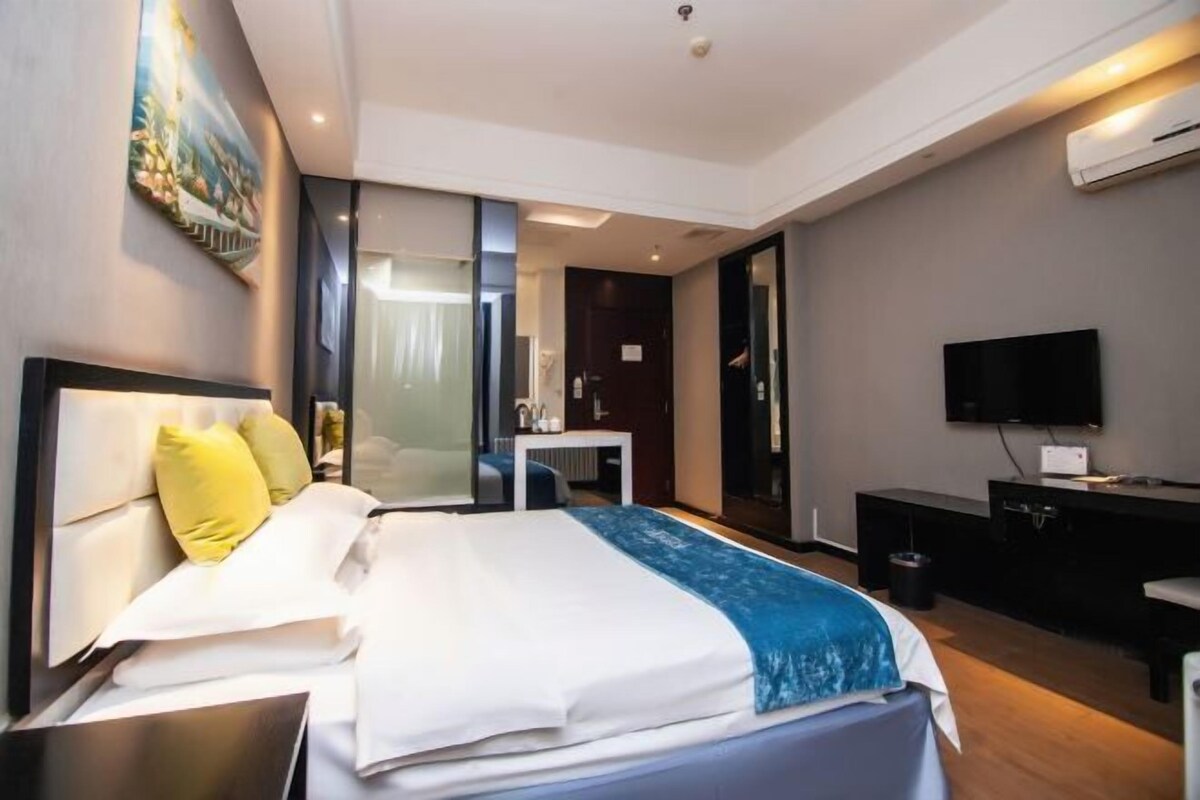 A modern hotel room with a bed, a desk, a television, and a painting on the wall.