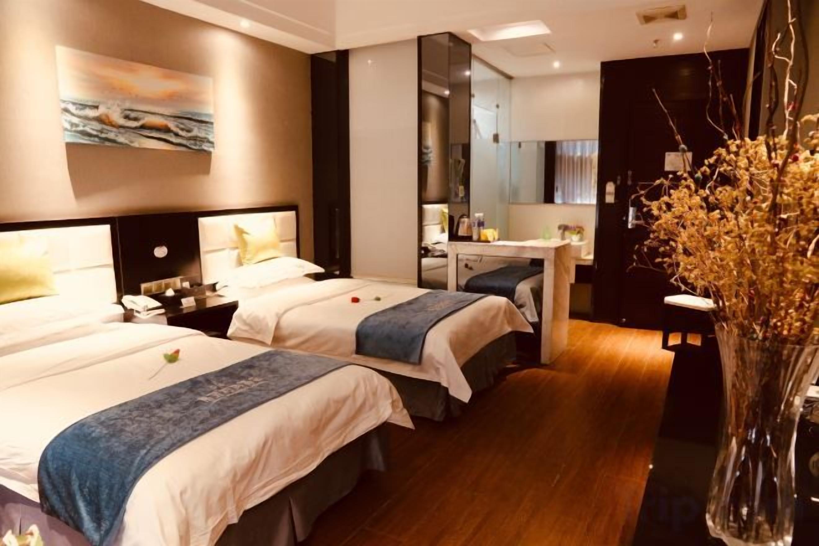 Habitación de hotel con dos camas, un escritorio, un espejo y un jarrón con flores secas.