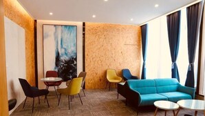 Ein moderner Lounge-Bereich mit einem blauen Sofa, gelben und schwarzen Sesseln, einem kleinen runden Tisch und einem großen abstrakten Gemälde an der Wand.