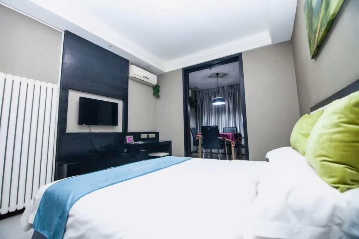 A hotel room with a bed, a desk, a chair, a TV, and a window with curtains.