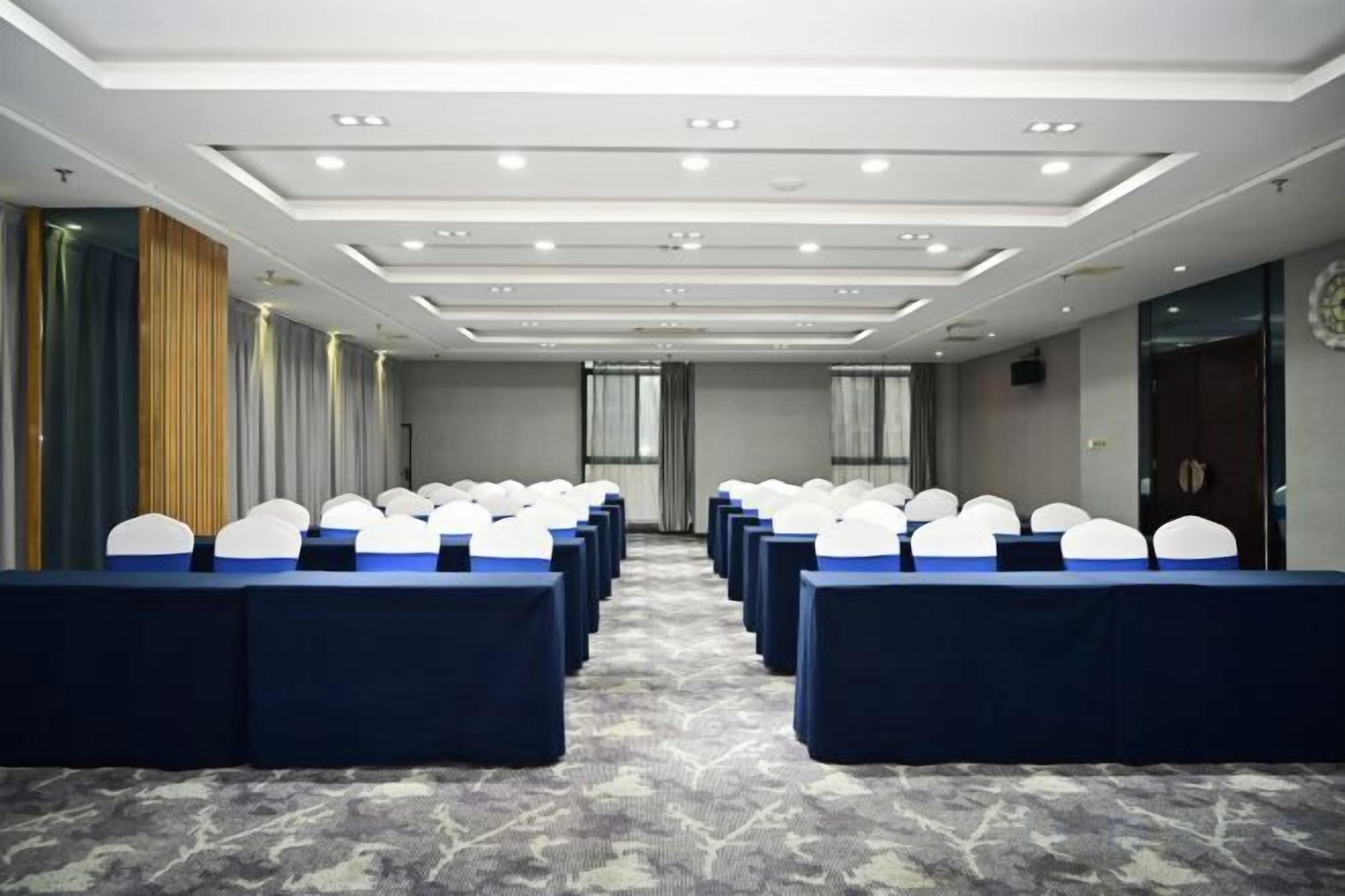 A conference room with rows of tables and chairs, a patterned carpet, and a modern ceiling design.