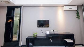 A modern hotel room with a flat-screen TV mounted on the wall, a black console table with a bench, and a small trash bin.