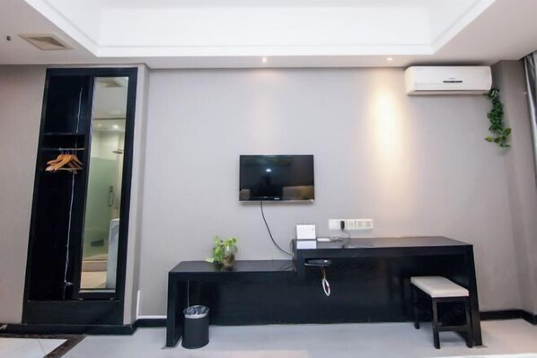 A modern hotel room with a flat-screen TV mounted on the wall, a black console table with a bench, and a small trash bin. - Yicheng Hotel (Henan University of Technology) (Zhengzhou)