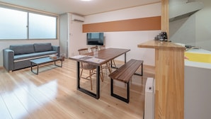 A modern living room with a sofa, a wooden dining table, and a kitchen area with a sink and stove. - Takayama Stay Karatachi DX-A (Takayama)