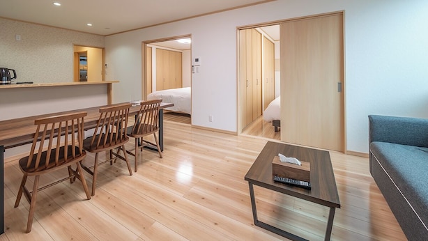 A modern, well-lit room with a wooden dining table, chairs, a sofa, and a small TV table. - Takayama Stay Karatachi DX-A (Takayama)